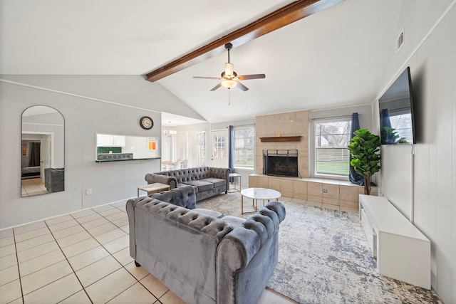 living room featuring ceiling fan, brick wall, lofted ceiling with beams, a tiled fireplace, and light tile patterned floors