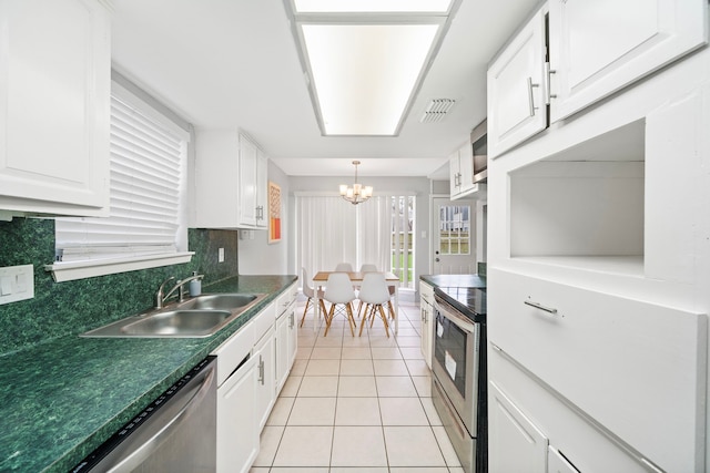 kitchen with dark countertops, appliances with stainless steel finishes, white cabinetry, a sink, and light tile patterned flooring