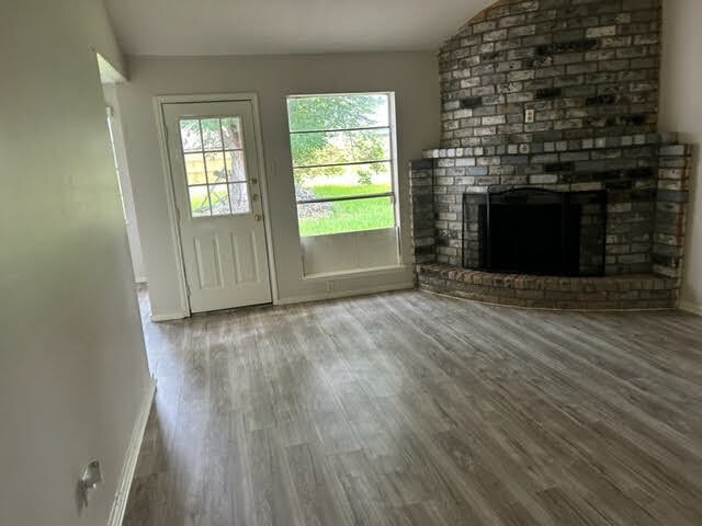 unfurnished living room with hardwood / wood-style flooring, lofted ceiling, and a brick fireplace