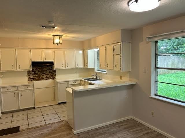 kitchen featuring a peninsula, light countertops, white cabinets, a sink, and light wood finished floors
