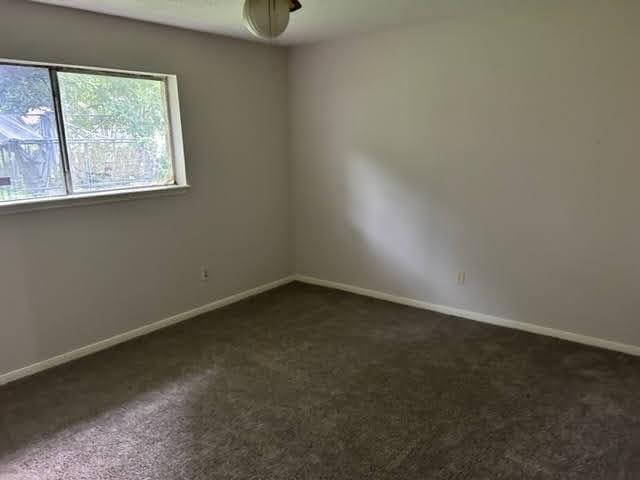 spare room with dark colored carpet, baseboards, and ceiling fan