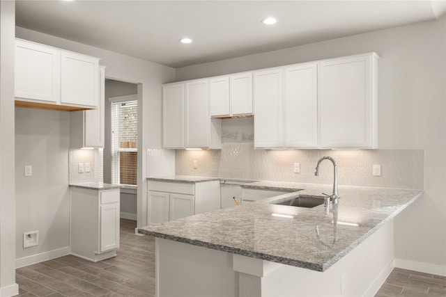 kitchen with hardwood / wood-style floors, white cabinetry, kitchen peninsula, and sink