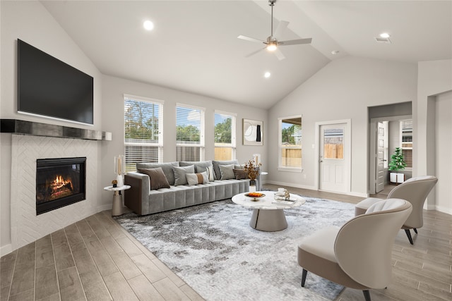 living room with light wood-type flooring, a tiled fireplace, ceiling fan, and high vaulted ceiling