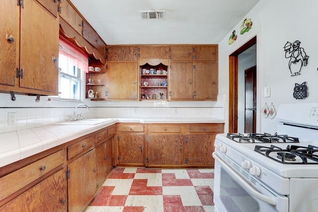 kitchen featuring tile counters, white range with gas cooktop, sink, and light tile patterned floors