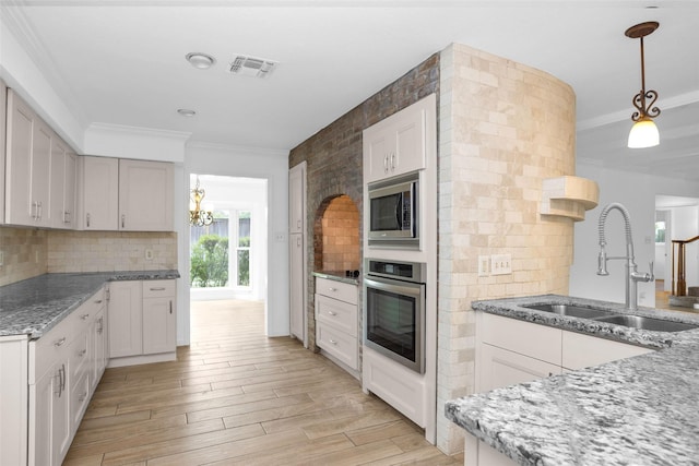 kitchen with visible vents, decorative light fixtures, light stone countertops, stainless steel appliances, and a sink