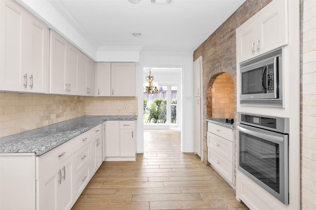 kitchen featuring decorative backsplash, light wood-style flooring, ornamental molding, stainless steel appliances, and white cabinetry