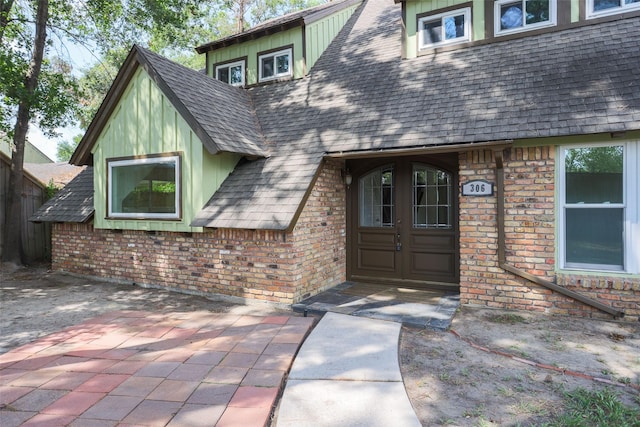 view of exterior entry with brick siding, a shingled roof, a patio area, and french doors