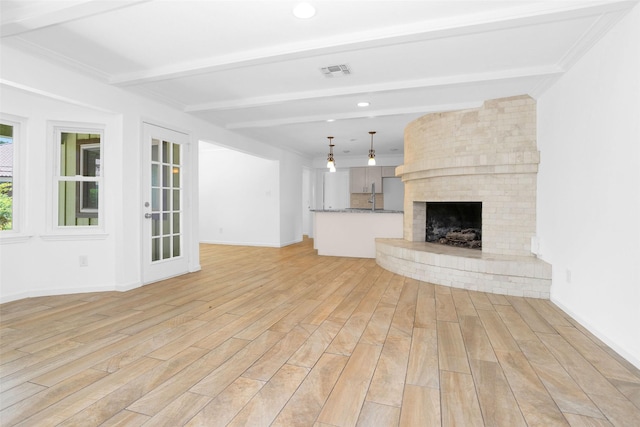 unfurnished living room featuring beam ceiling, a fireplace, visible vents, light wood-style flooring, and baseboards