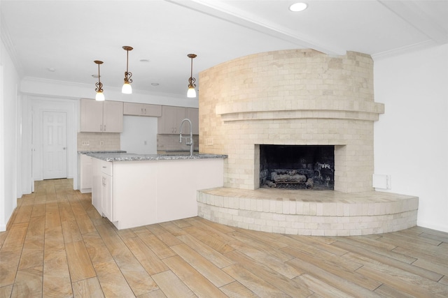 kitchen featuring light stone counters, pendant lighting, ornamental molding, and light wood finished floors