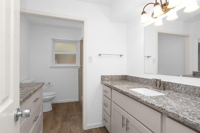 bathroom featuring baseboards, toilet, wood finished floors, an inviting chandelier, and vanity