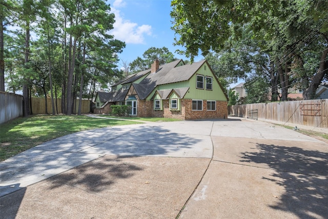 view of front facade with brick siding, a chimney, a front yard, and a fenced backyard