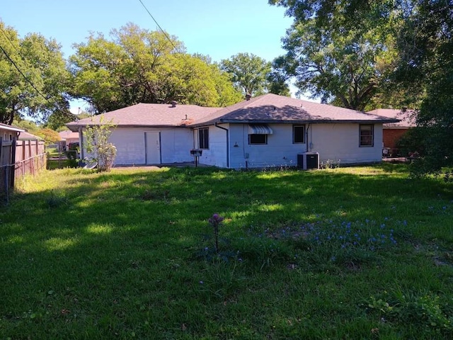 rear view of property featuring central air condition unit and a lawn