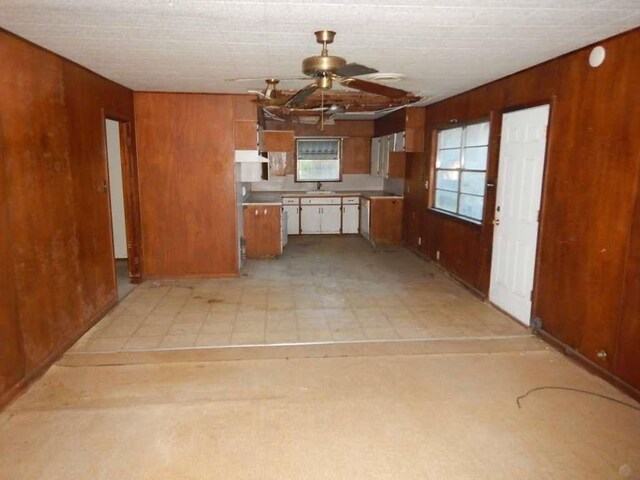 kitchen with light tile patterned flooring, wooden walls, sink, and ceiling fan