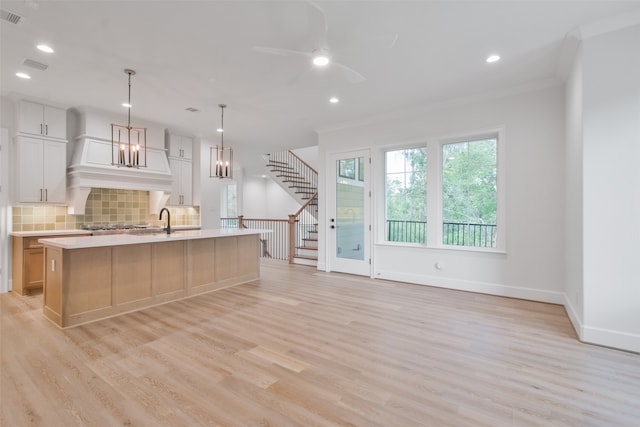 kitchen featuring tasteful backsplash, an island with sink, sink, light hardwood / wood-style flooring, and white cabinets