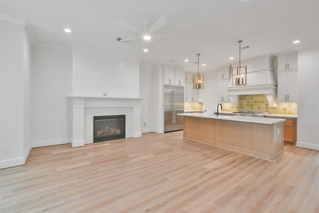 kitchen with light wood-type flooring, a kitchen island with sink, sink, white cabinets, and built in fridge