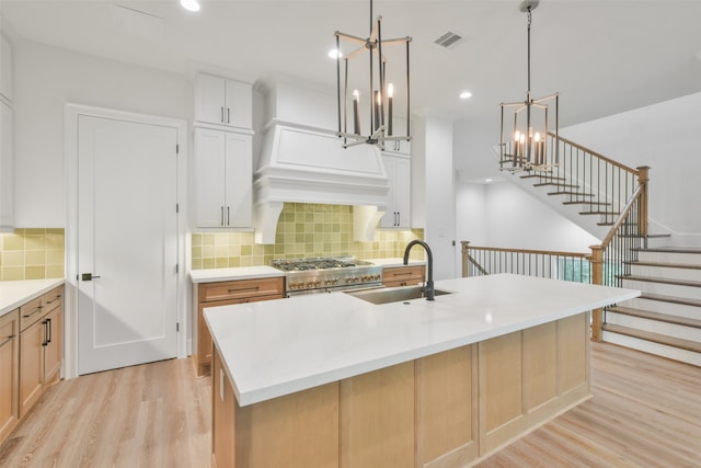 kitchen featuring range with two ovens, white cabinets, an island with sink, and light wood-type flooring