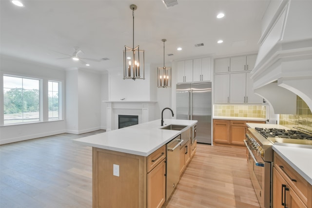 kitchen featuring light hardwood / wood-style flooring, white cabinetry, premium appliances, an island with sink, and tasteful backsplash