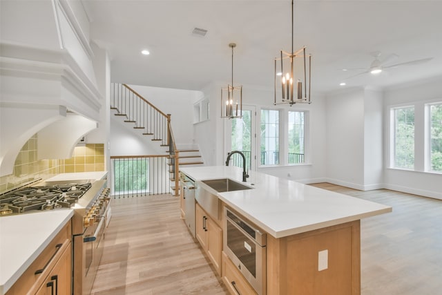 kitchen featuring stainless steel appliances, ceiling fan with notable chandelier, a kitchen island with sink, light wood-type flooring, and sink