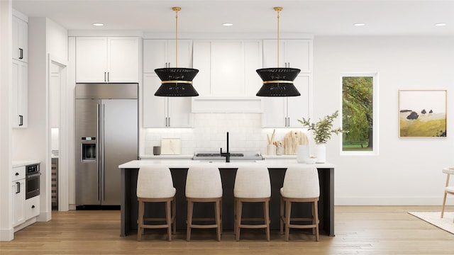 kitchen featuring decorative light fixtures, stainless steel appliances, white cabinets, and a center island with sink