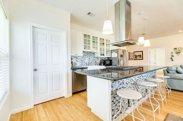 kitchen with appliances with stainless steel finishes, island range hood, decorative light fixtures, white cabinetry, and a kitchen bar