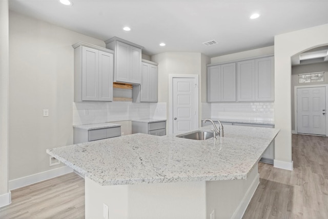 kitchen with backsplash, gray cabinets, sink, and an island with sink