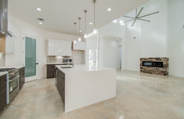 kitchen with tasteful backsplash, an island with sink, high end stainless steel range oven, wall chimney exhaust hood, and pendant lighting