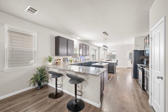 kitchen featuring light hardwood / wood-style flooring, pendant lighting, kitchen peninsula, dark brown cabinets, and gas stove