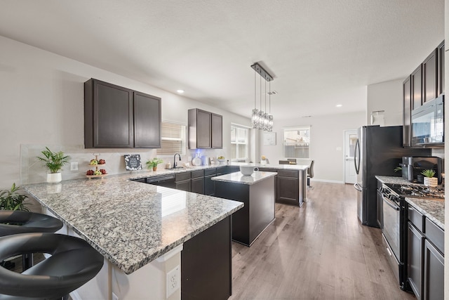 kitchen featuring kitchen peninsula, a kitchen island, stainless steel appliances, light hardwood / wood-style floors, and hanging light fixtures