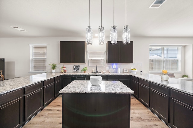 kitchen featuring light hardwood / wood-style floors, light stone countertops, hanging light fixtures, and sink