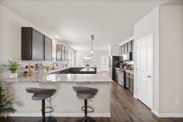 kitchen with appliances with stainless steel finishes, kitchen peninsula, hardwood / wood-style floors, and decorative light fixtures