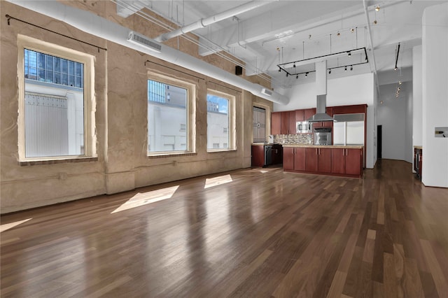 unfurnished living room with track lighting, dark wood-type flooring, and a high ceiling