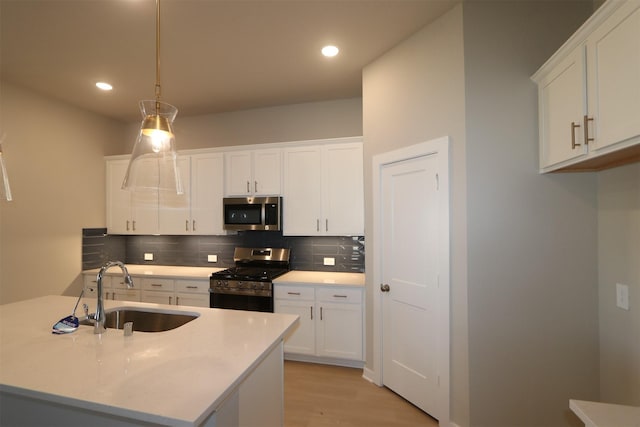 kitchen featuring appliances with stainless steel finishes, white cabinetry, sink, hanging light fixtures, and light hardwood / wood-style floors