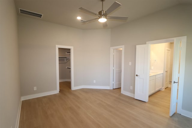 unfurnished bedroom with a walk in closet, light hardwood / wood-style flooring, ensuite bath, ceiling fan, and a closet