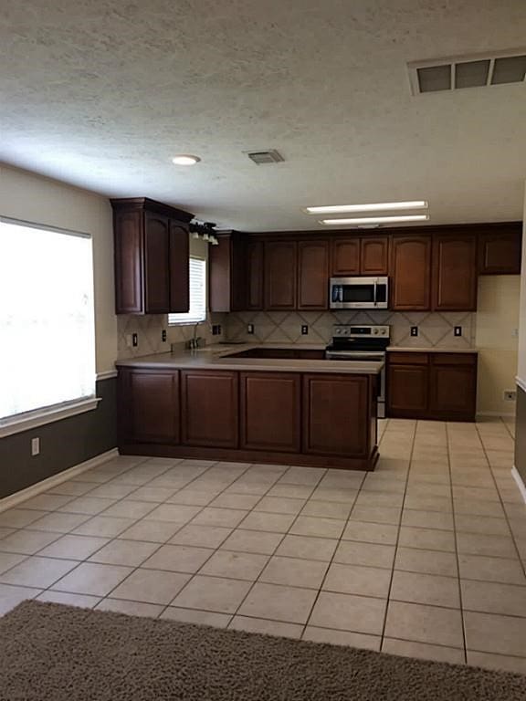 kitchen featuring light tile patterned flooring, dark brown cabinets, decorative backsplash, and appliances with stainless steel finishes