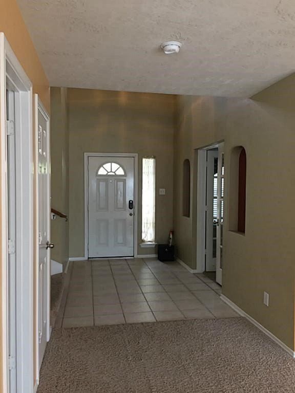 carpeted foyer entrance with a textured ceiling