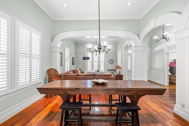 dining room with ornate columns, crown molding, wood-type flooring, and a notable chandelier