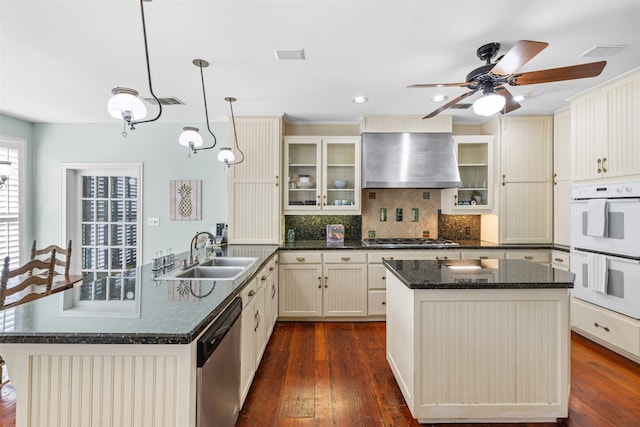 kitchen with dark hardwood / wood-style floors, stainless steel appliances, wall chimney exhaust hood, sink, and hanging light fixtures