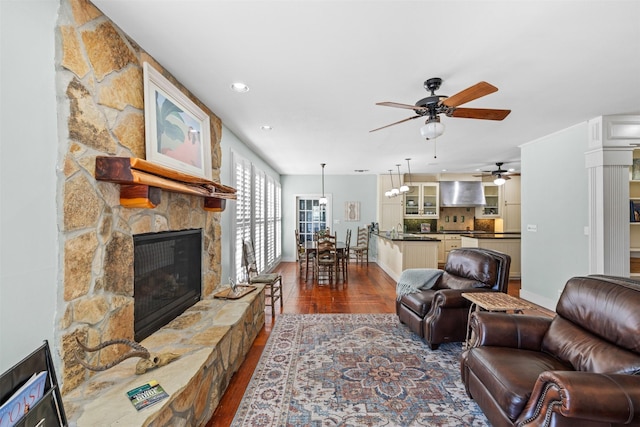 living room featuring dark wood-type flooring, ceiling fan, a stone fireplace, and sink