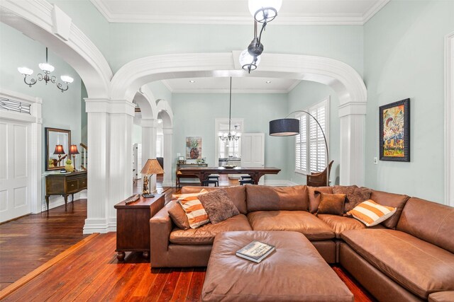 living room featuring a towering ceiling, decorative columns, dark hardwood / wood-style flooring, crown molding, and an inviting chandelier