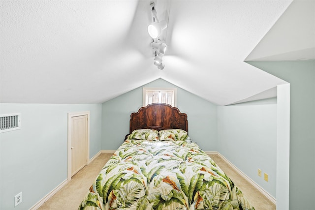 carpeted bedroom with track lighting, vaulted ceiling, and a textured ceiling