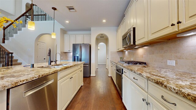 kitchen with sink, hanging light fixtures, appliances with stainless steel finishes, dark hardwood / wood-style flooring, and light stone counters