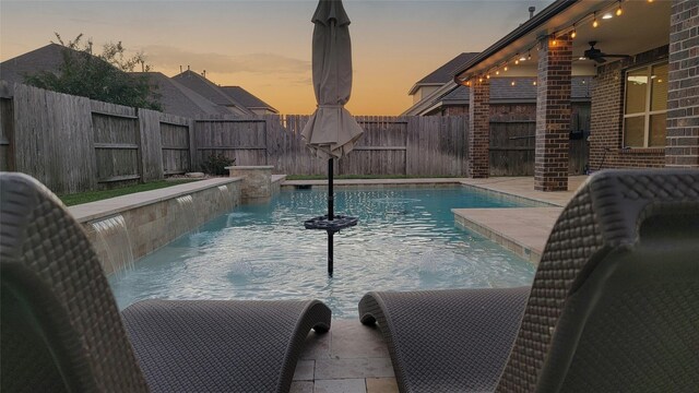 pool at dusk featuring pool water feature and ceiling fan