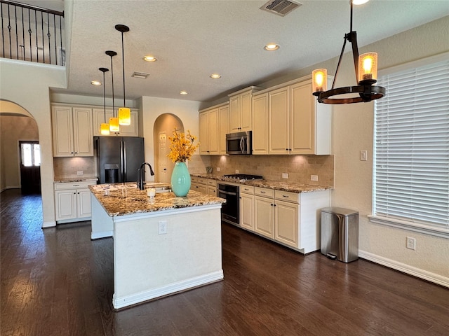 kitchen featuring a center island with sink, backsplash, hanging light fixtures, light stone countertops, and black appliances