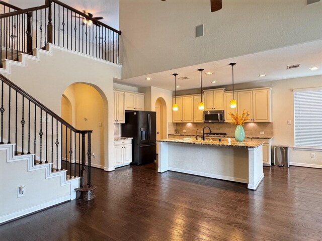 kitchen featuring light stone countertops, black refrigerator with ice dispenser, an island with sink, tasteful backsplash, and hanging light fixtures