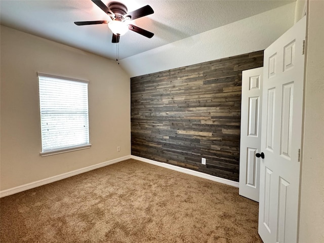 carpeted empty room with ceiling fan, a textured ceiling, wood walls, and vaulted ceiling