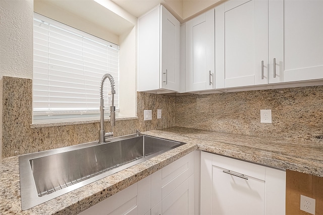 kitchen with sink, white cabinets, tasteful backsplash, and light stone counters