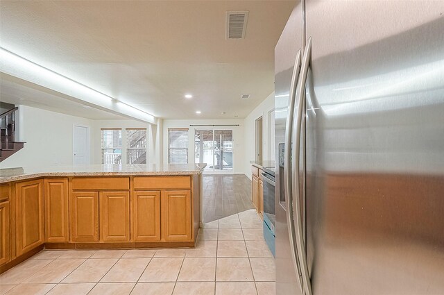 kitchen with light tile patterned flooring, light stone countertops, kitchen peninsula, and stainless steel appliances