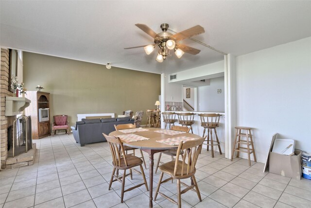 dining room featuring ceiling fan, light tile patterned floors, and a brick fireplace