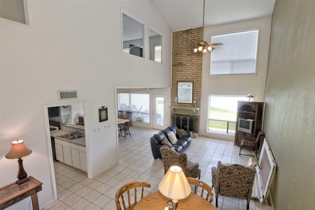 living area featuring light tile patterned flooring, a brick fireplace, a towering ceiling, and visible vents