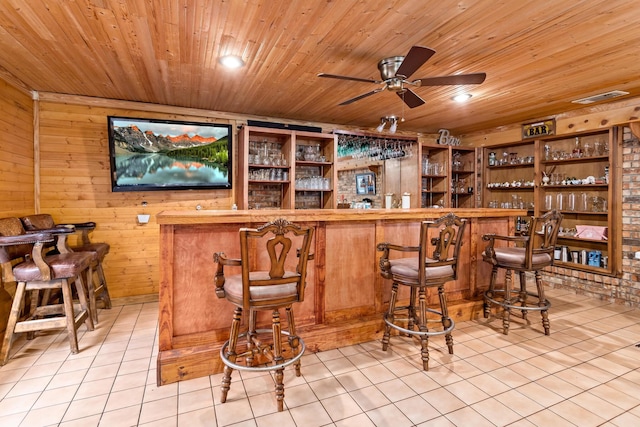 bar with ceiling fan, wooden ceiling, wooden walls, and light tile patterned flooring